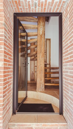 Une porte qui mène à une pièce dont les poutres en bois et les murs en briques sont apparents.