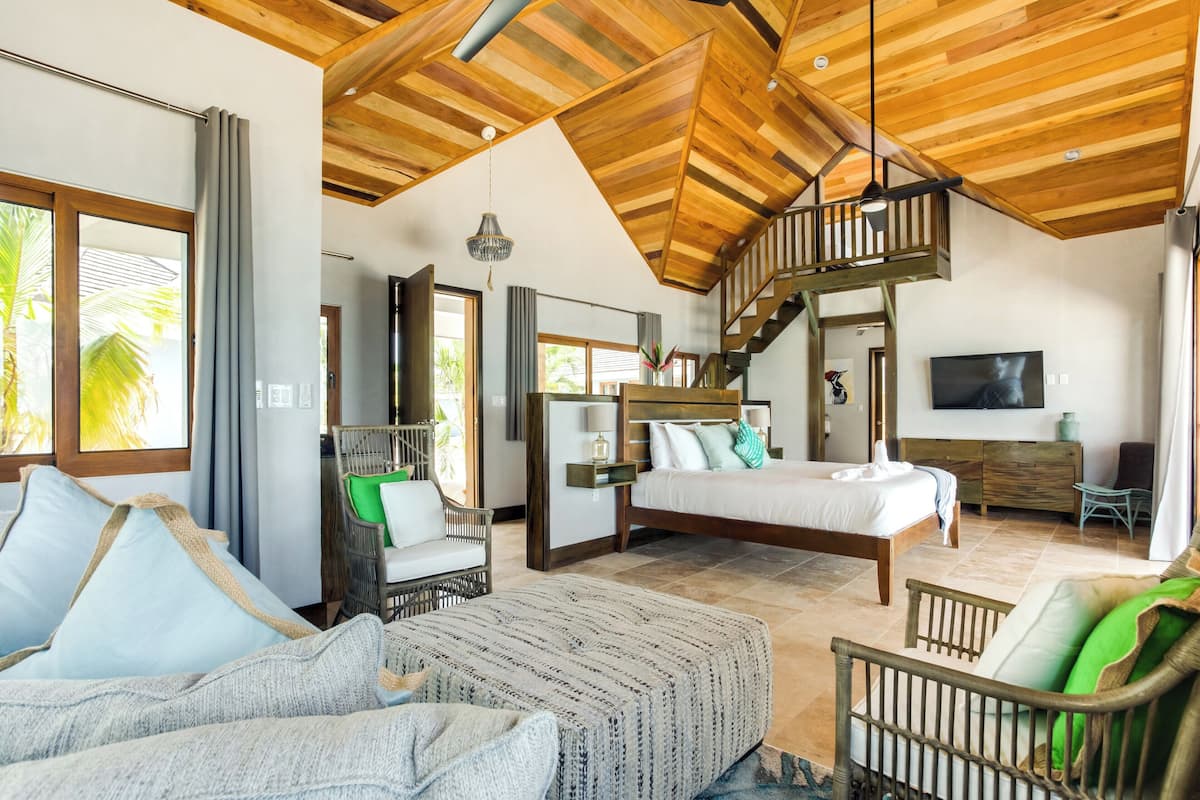 A spacious bedroom with a large bed, a wooden staircase, and a balcony.