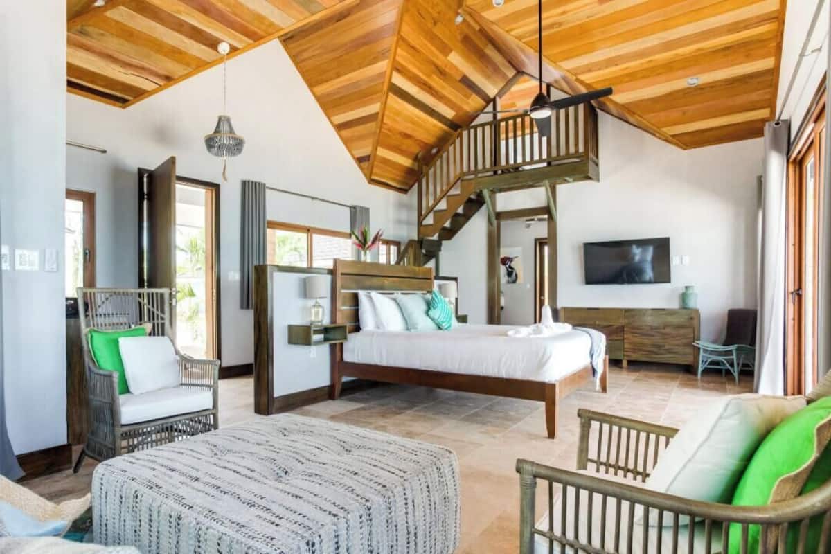 A spacious room with a high ceiling, a bed, a sofa, and a staircase leading to an upper level.