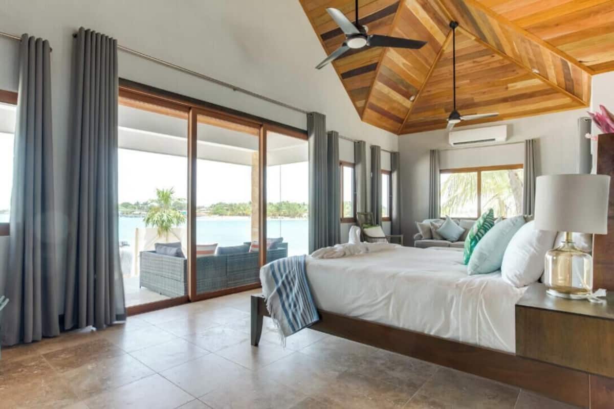 A spacious bedroom with a large bed, a bench, and a view of the sea.