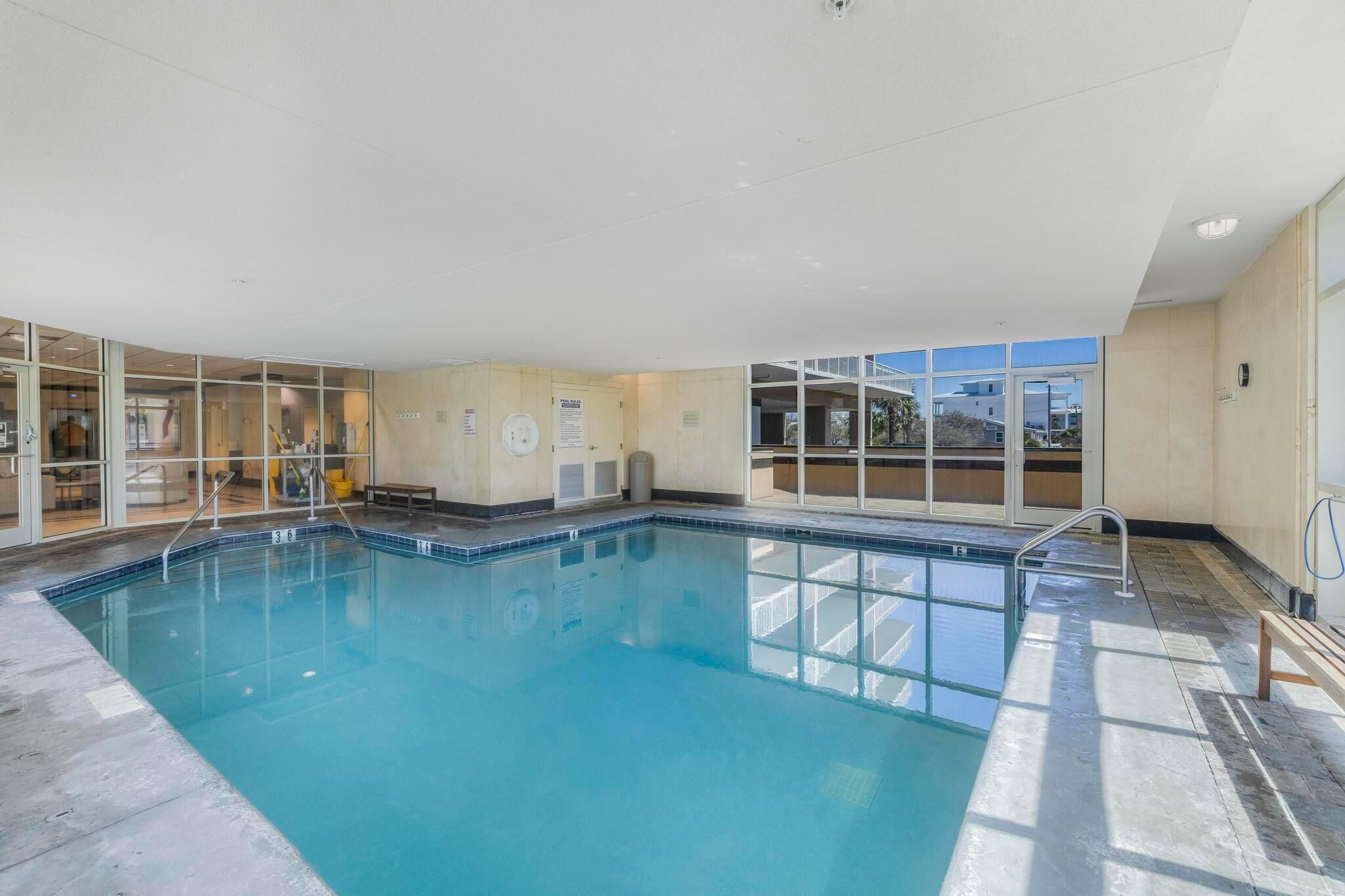 Une piscine intérieure avec des parois en verre transparent, un sol carrelé et un banc au bord du bassin.