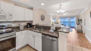 A modern kitchen with white cabinets, granite countertops, stainless steel appliances, and a view to the outside. - Crystal Tower 906 (Gulf Shores)
