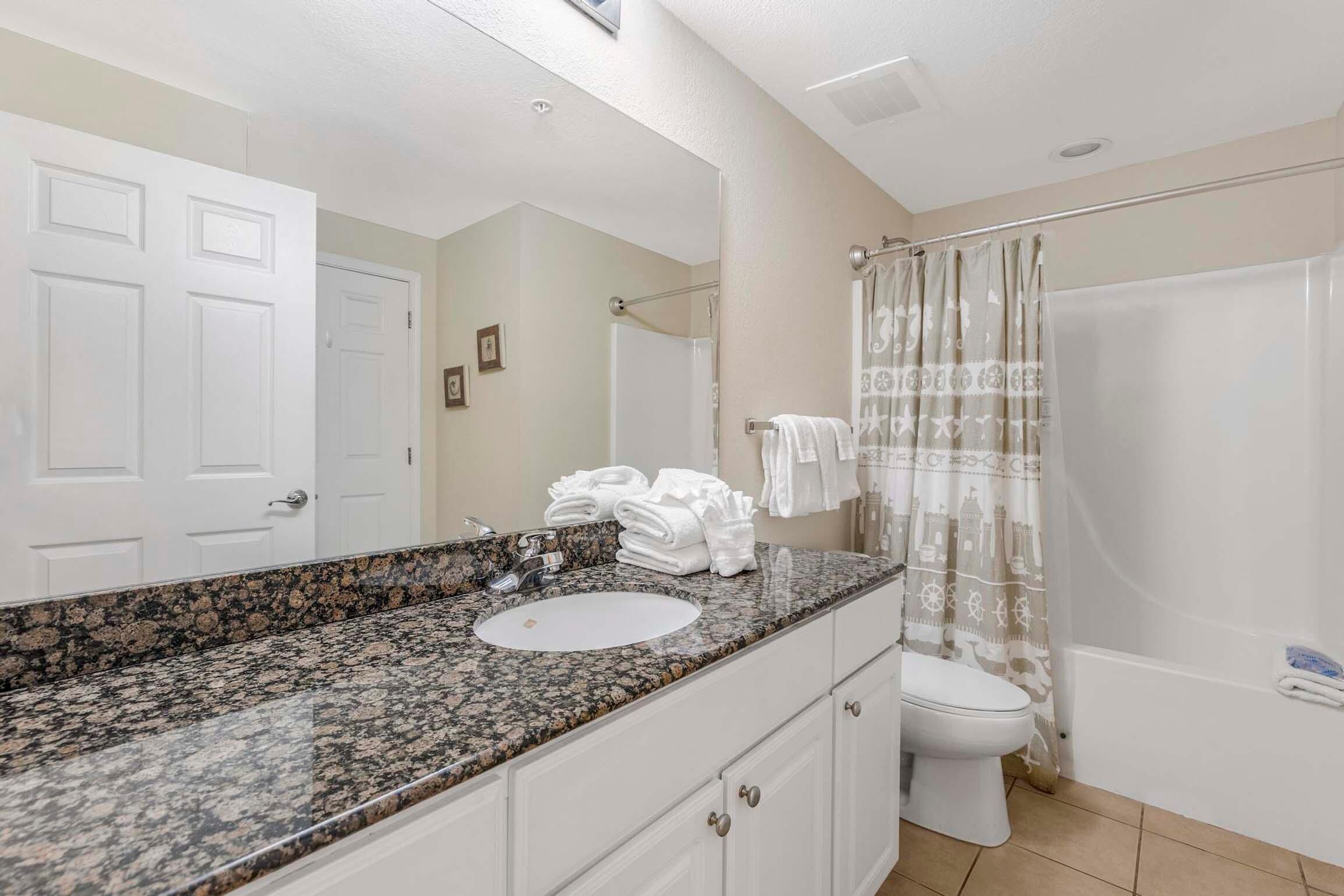 A bathroom with a granite countertop sink, a toilet, and a shower with a patterned curtain.