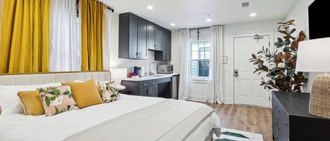 A bedroom with a large bed, a desk, and a kitchenette.