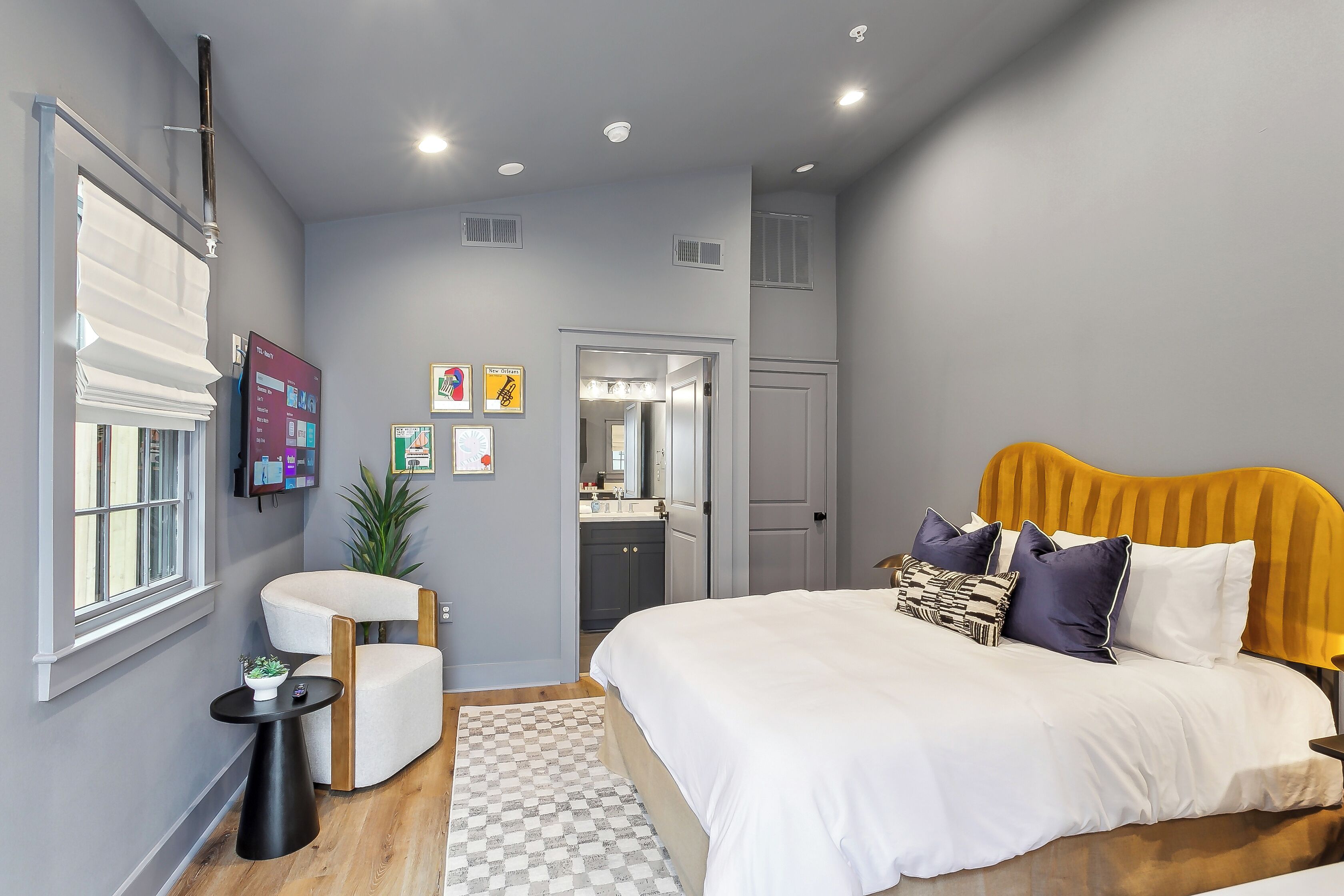 A modern bedroom with a large bed, a bedside table, a chair, and a small table with a plant.