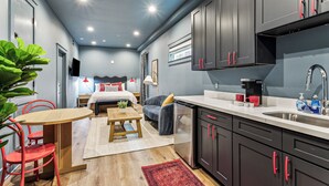 A compact hotel room with a kitchenette, a bed with a headboard, a dining area with a table and chairs, and a large potted plant. - Vibrant NOLA Retreat Jazz & Culture (New Orleans)