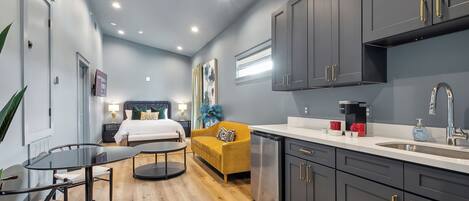 A modern hotel room with a bed, a yellow sofa, a dining table, and a kitchenette.