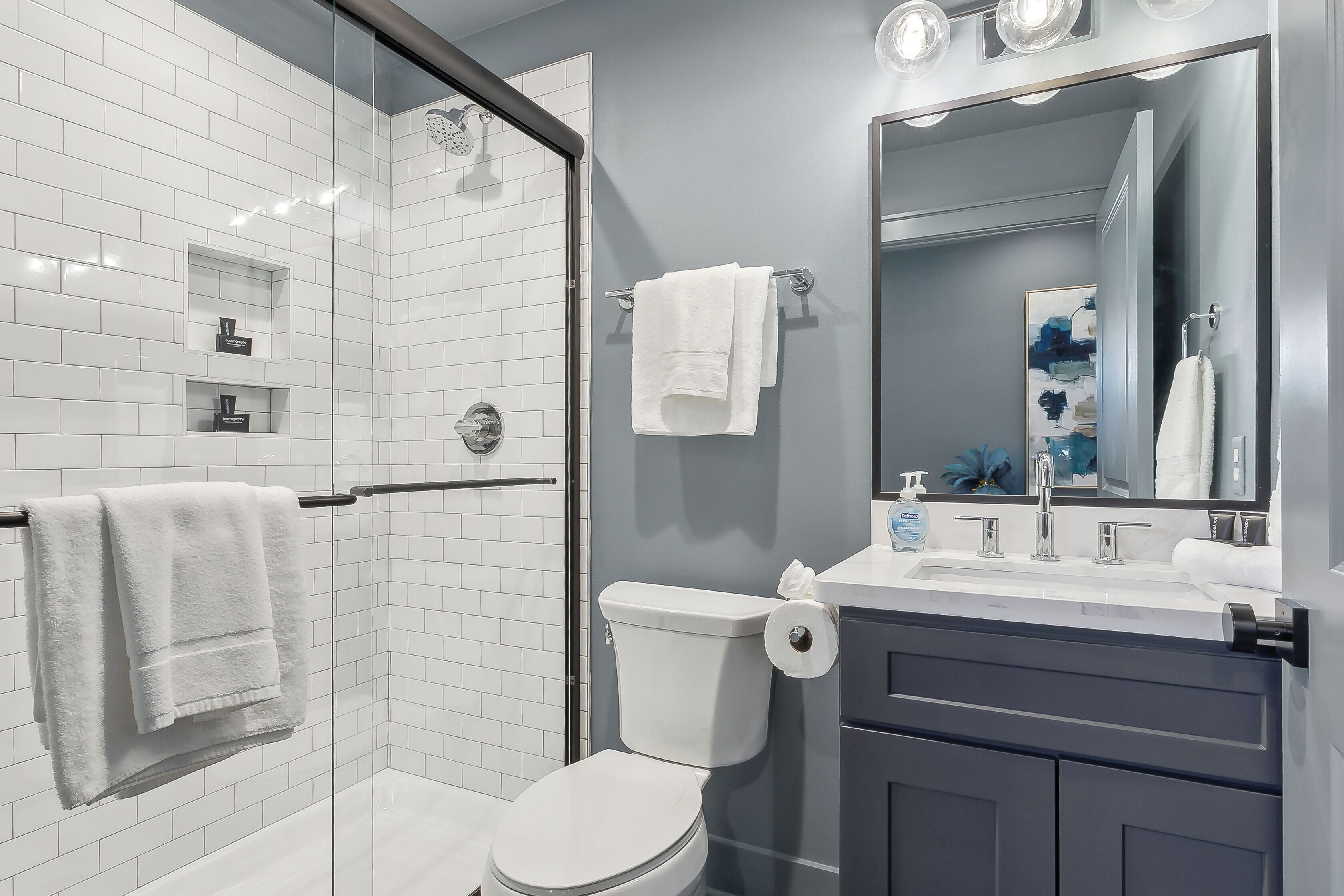 Een moderne badkamer met een douchecabine van glas, een wit toilet en een wastafel met een spiegel.