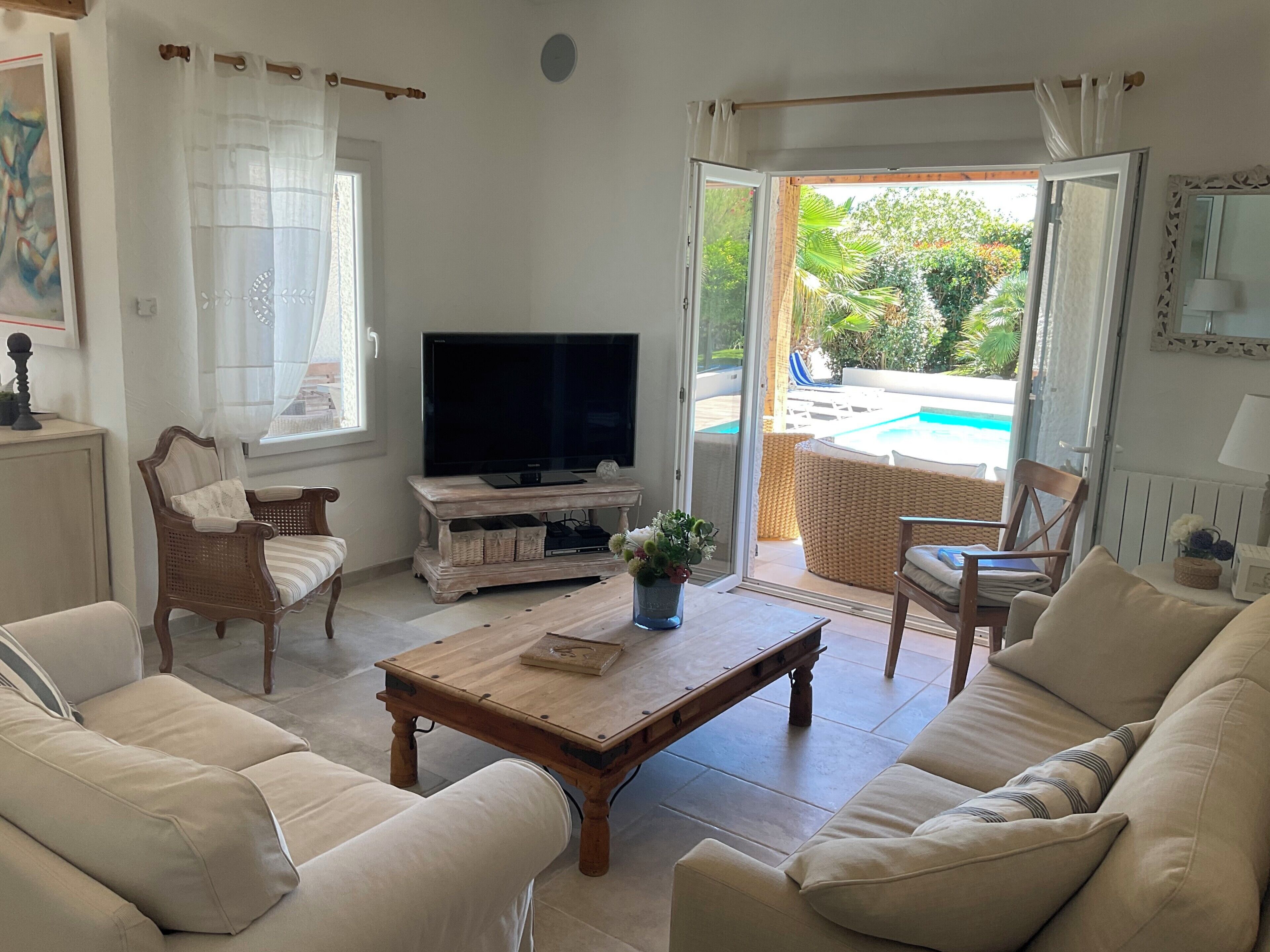 A living room with a TV, sofas, a coffee table, and a view of a pool.