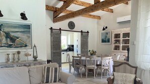 A spacious living area with a sofa, dining table, and chairs. A kitchen is visible in the background. - LVAM – Villa Maraval · 8 Guests · 4 Bedrooms · Swimming Pool (Agde)