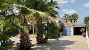 A courtyard with palm trees, a pool, and a building with a tiled roof. - LVAM – Villa Maraval · 8 Guests · 4 Bedrooms · Swimming Pool (Agde)