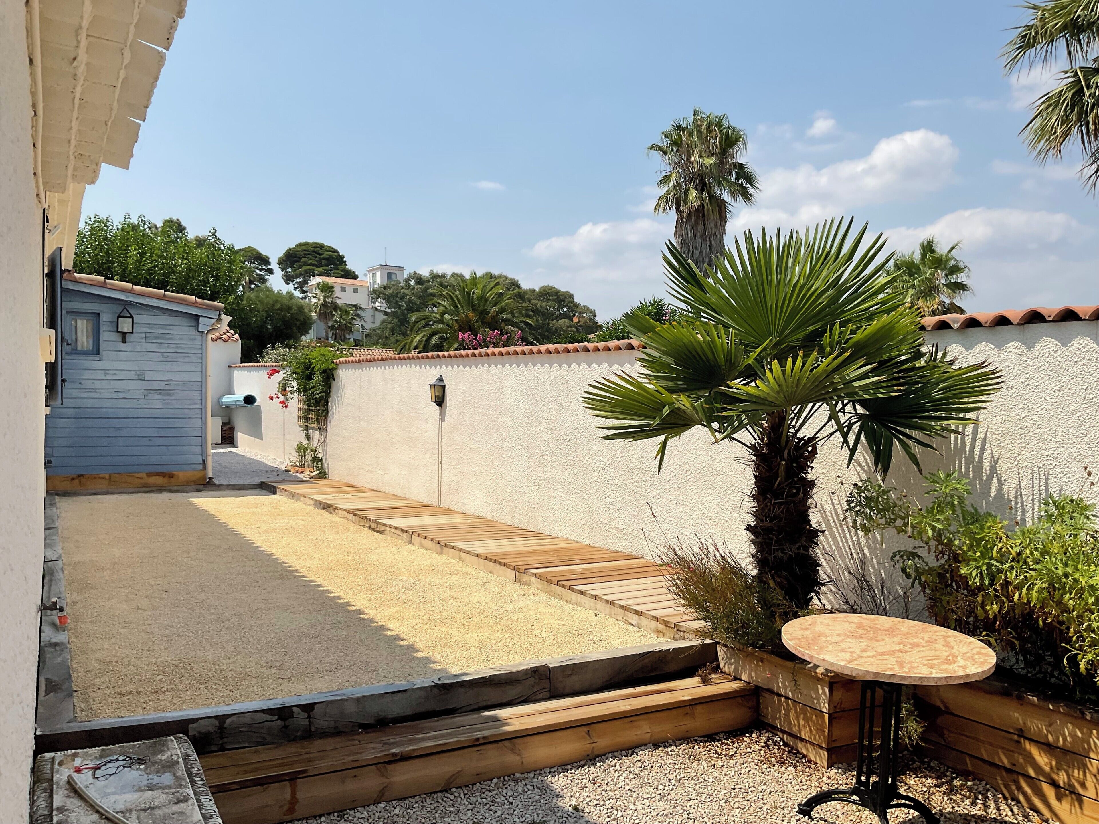A courtyard with a wooden deck, a palm tree, and a small round table.