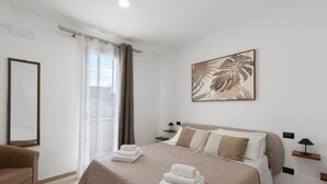 A hotel room with a bed, a chair, a bedside table, a lamp, a painting, and a window with curtains. - Room '2' with Balcony, Wi-Fi and Air Conditioning (Balestrate)