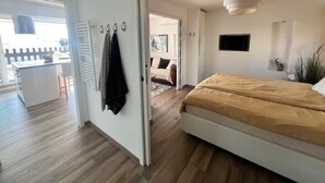 A modern bedroom with a large bed, a TV, and a dining area with a kitchen in the background. - Naturiste Cap d'Agde Villa Port Nature 187 (Agde)