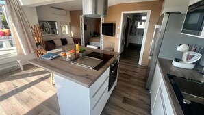 A modern kitchen with a central island, built-in appliances, and a view to the dining area. - Naturiste Cap d'Agde Villa Port Nature 187 (Agde)