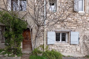 Ein rustikales Steinhaus mit Holztür, einem Fenster mit Fensterläden und einem kleinen Garten.