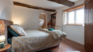 Een slaapkamer met een bed, een nachtkastje, een raam en een houten balk.