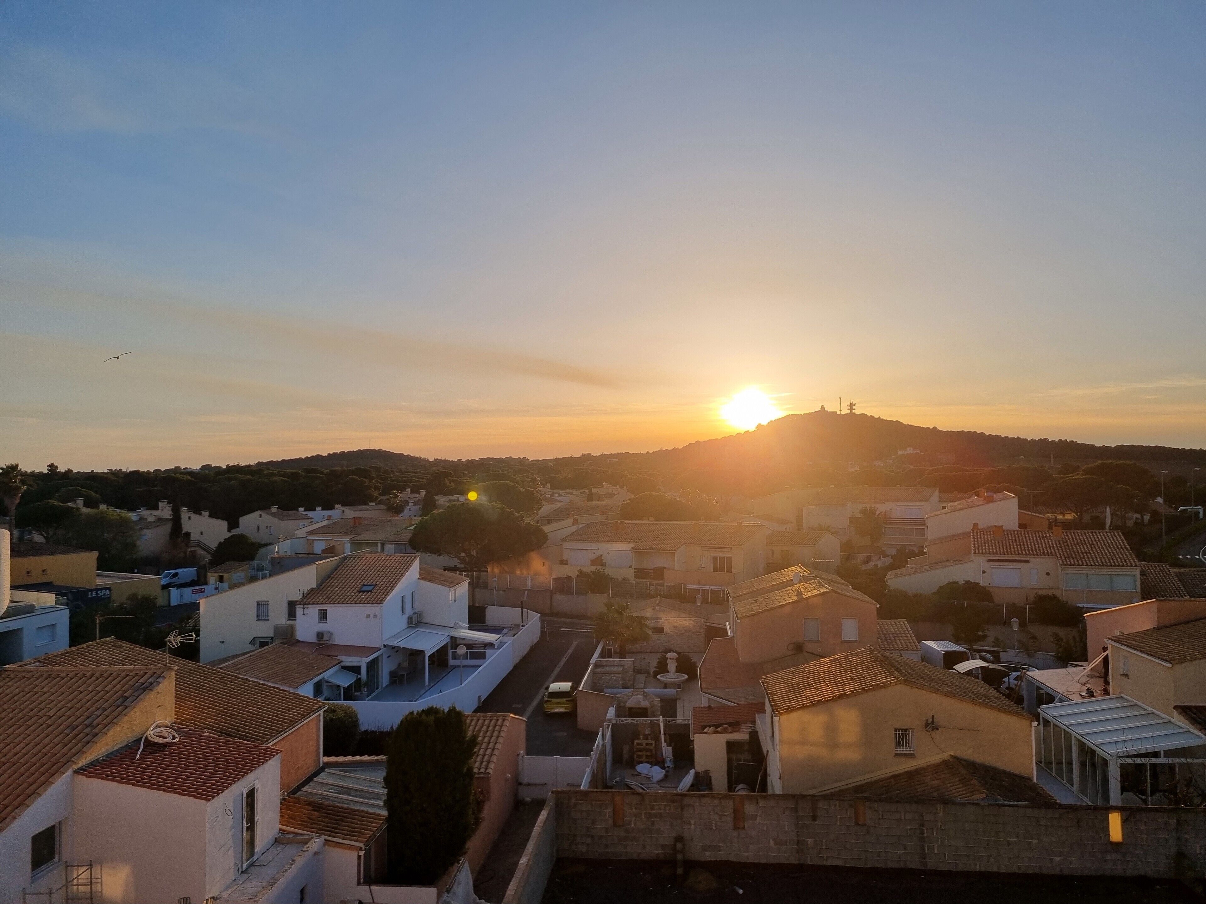 Un barrio residencial con casas, cielo despejado y el sol poniéndose al fondo.
