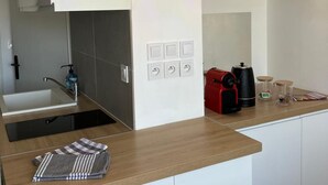 Une cuisine moderne équipée d’un évier encastré, d’une machine à café et d’une bouilloire posées sur le plan de travail.