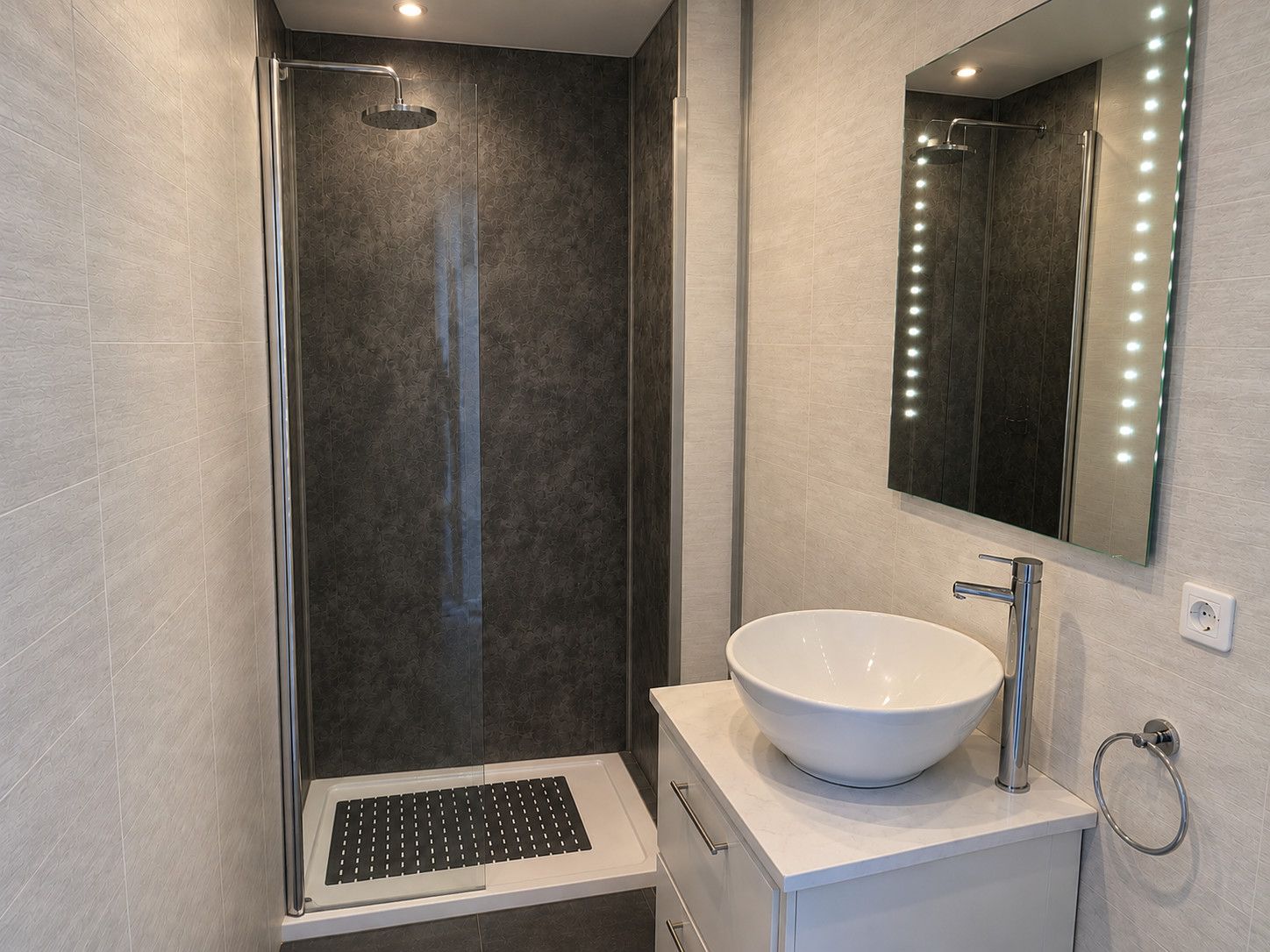 A modern bathroom with a walk-in shower, a large mirror with lights, and a white sink.