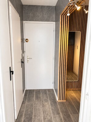 A hallway with a white door, a wooden slatted wall, and a tiled floor. - Naturiste Cap d'Agde Héliopolis F 90 (Agde)