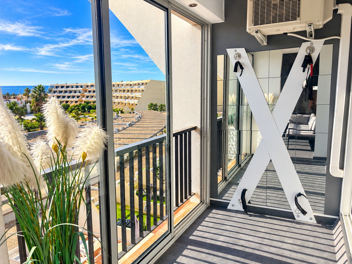 Een balkon met uitzicht op een hotelcomplex, een grote 'X'-decoratie en een bloempot met een plant.