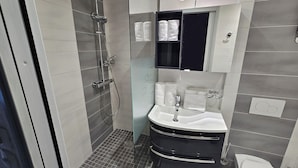 A modern bathroom with a glass-enclosed shower, a black vanity with a white sink, and neatly arranged towels. - Naturiste Cap d'Agde Villa Héliovillage 20 (Agde)