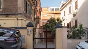 Une rue étroite, bordée de bâtiments des deux côtés, avec une entrée fermée par un portail et des voitures garées.