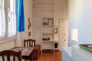 Um quarto com uma mesa de jantar, cadeiras, uma estante e uma janela com cortinas.