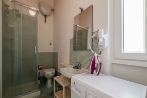 Casa de banho com cabine de chuveiro em vidro, sanita, lavatório e espelho.