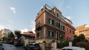Un immeuble à plusieurs étages, doté d’une entrée fermée par un portail, avec des voitures garées et un ciel dégagé.
