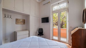 Une chambre avec un lit, une chaise, un téléviseur et une porte-fenêtre coulissante donnant sur l’extérieur.