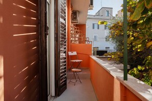 Un balcón estrecho con una silla, una mesita y una ventana con persianas.