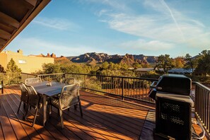 Eine Holzterrasse mit Tisch, Stühlen, einem Grill und Blick auf Berge.