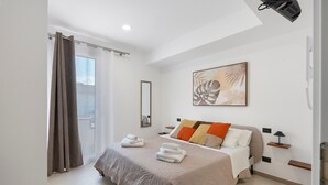 Une chambre d’hôtel moderne dotée d’un grand lit, d’un projecteur fixé au plafond et d’une porte-fenêtre coulissante donnant sur l’extérieur.