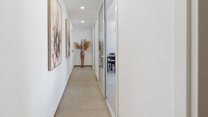 Un couloir orné de tableaux encadrés, avec une plante en pot et un coin repas visible à travers une cloison vitrée.