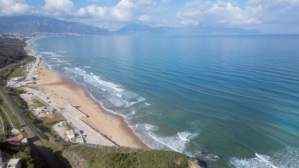 Un paysage côtier avec une plage, une route et des montagnes à l’horizon.