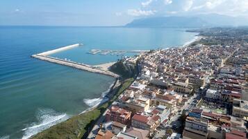 Una veduta aerea di una città costiera con un porto turistico, una zona urbana densa e un molo frangiflutti ben visibile.