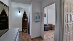 Ein Flur mit einem schiffsförmigen Regal aus Holz, einer Wanddekoration und einem Bett mit grauer Bettdecke.