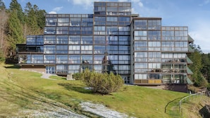 A modern multi-story building with large glass windows and a flat roof, surrounded by a grassy area and trees. - Lodge Belle Hutte - Proche des Pistes (La Bresse)