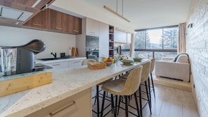 A modern kitchen with a marble countertop, wooden cabinets, and a built-in oven. There is a dining area with a table and chairs, and a view of the outdoors through large windows. - Lodge Belle Hutte - Proche des Pistes (La Bresse)