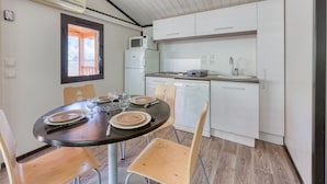 A compact kitchen with white cabinets, a microwave, and a dining area with a round table set for two. - Lou Pitchoun - Cottage pour 5 (Solliès-Toucas)