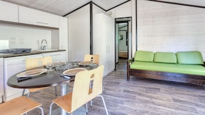 A modern kitchen with white cabinets, a dining table set with plates and glasses, and a green sofa in the living area. - Lou Pitchoun - Cottage pour 5 (Solliès-Toucas)