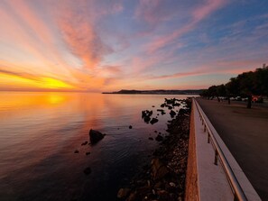 A coastal sunset view with a paved walkway along the shore. - Comfortable apartment 50m from the beach (L'Escala)