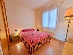 A bedroom with a bed, a nightstand, a lamp, and a window with curtains. - Comfortable apartment 50m from the beach (L'Escala)