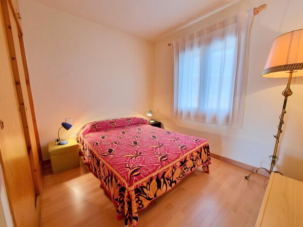 A bedroom with a bed, a nightstand, a lamp, and a window with curtains. - Comfortable apartment 50m from the beach (L'Escala)