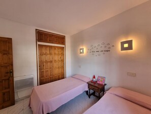 A bedroom with two beds, a wooden wardrobe, a wall-mounted light, and a decorative wall art piece.