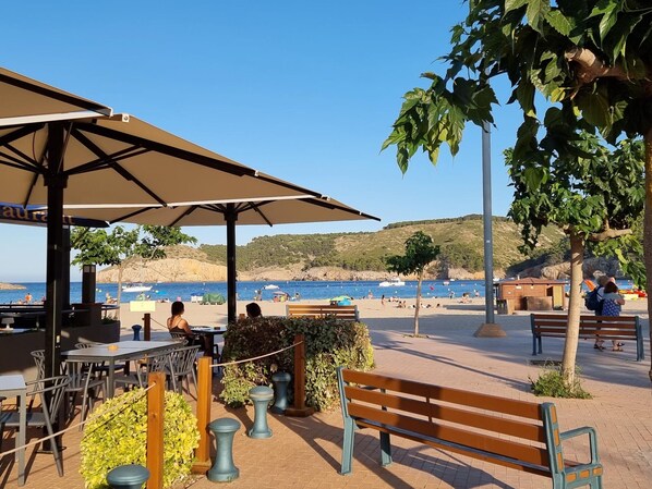 A seaside café with outdoor seating, a view of the beach, and a rocky coastline.