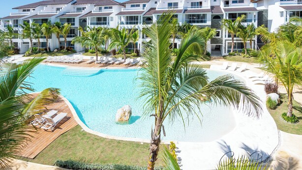 Un resort con una piscina grande, palmeras y un edificio de varios pisos con balcones.