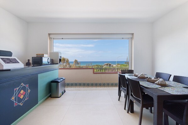 A balcony with a dining table and chairs, a microwave, and a trash bin.